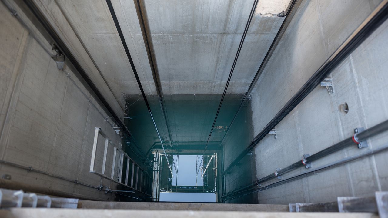 A deep industrial elevator shaft flooded with standing water, viewed from a high vantage point above.